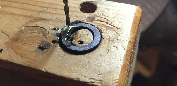 stainless steel chainmail ring on a piece of scrap wood with oil for lubrication, ready for the hole to be drilled